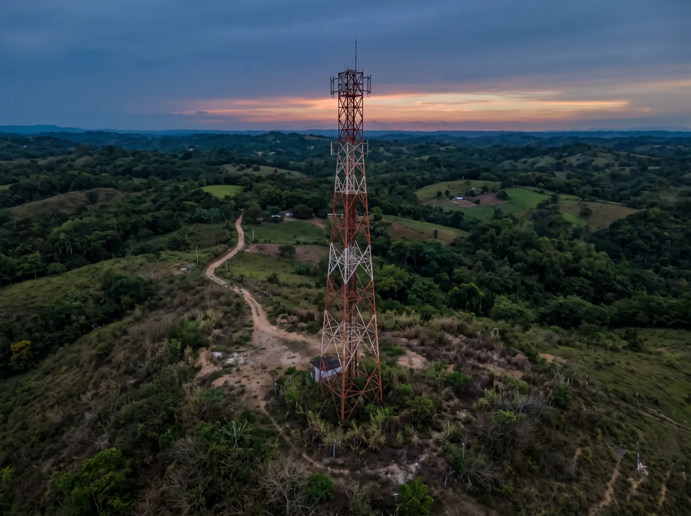 Sitio de telecomunicaciones desatendido al anochecer: torre sin cerramiento, sin luces