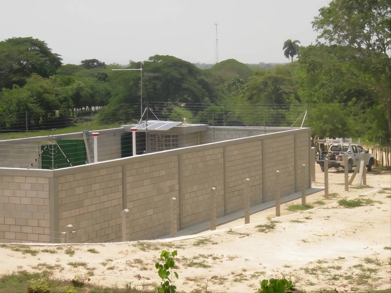 Cerramiento perimetral en bloque de concreto con cerca electrificada en la corona, protegiendo una estación remota.